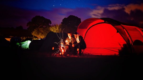 camping couple sitting by bonfire outside tent